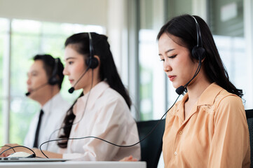 Team of call center staff in Asia wears headphones with a microphone. Smile while serving customers at desks and computers. Service concept and consulting. Communication concept.