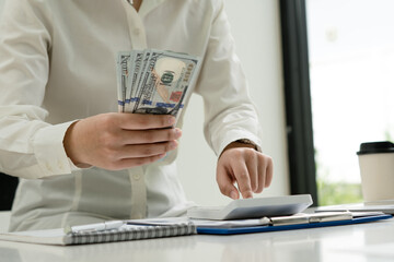 Fototapeta premium Investors are calculating on calculator investment costs and holding cash notes in hand.