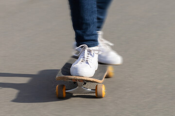 closeup female feet in white sneakers on skateboard on asphalt, on track. woman legs on board at skatepark. urban active extreme sport in the city. soft focus