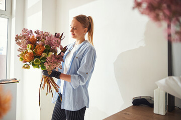 Smiling floral arranger admiring a spring bouquet in her hands - obrazy, fototapety, plakaty