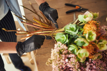 Experienced florist wrapping a bouquet with a string - obrazy, fototapety, plakaty
