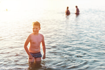 Cute young boy enjoy having fun at lake or river beach water on warm sunset evening time outdoors.