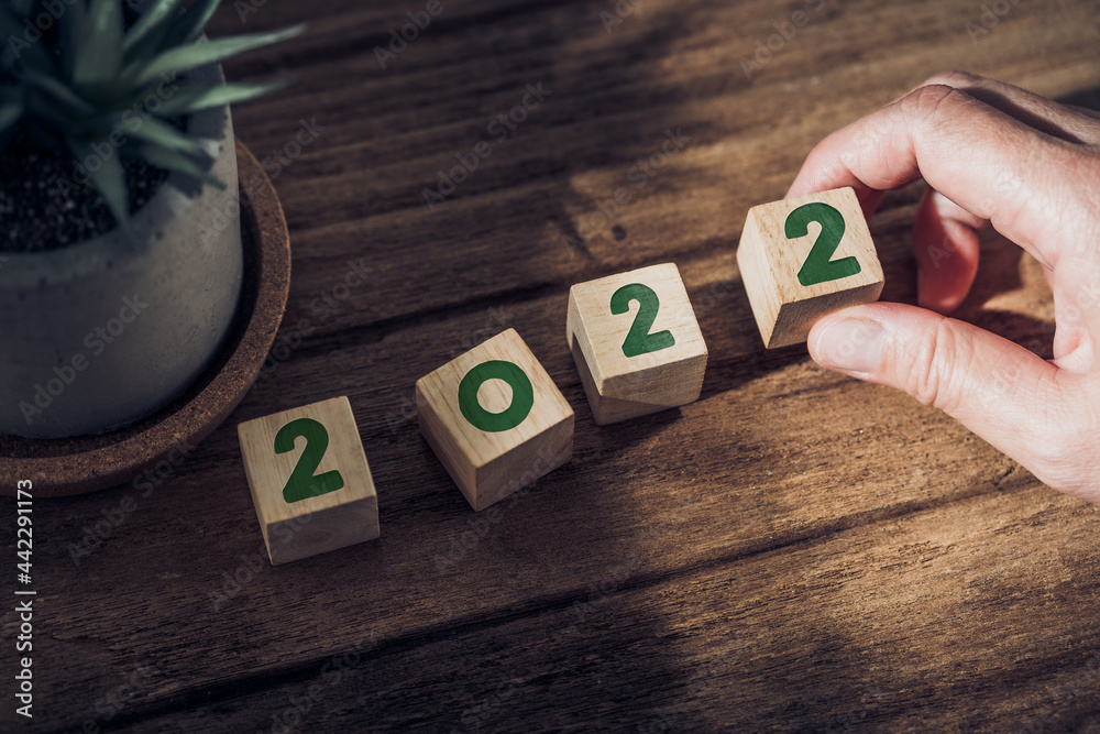 Poster 2022 happy new year with hand pick up wood block on wood table with sunlight from window.hope for new year concept