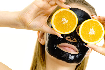 Girl black carbo mask on face holds orange fruit