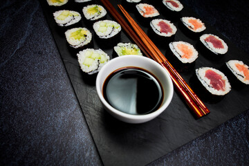 Bowl of soy juice on a chalkboard next to fish sushi and vegetable sushi and chopsticks. Japanese culture