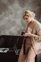 Young beautiful woman blogger in a modern loft interior. Woman photographer freelancer in beige stylish clothes looks at the camera screen.Soft selective focus.