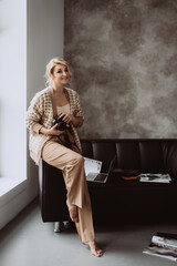 Young beautiful woman blogger in a modern loft interior. Woman freelance photographer in beige clothes smiling with a camera in her hands. Soft selective focus.