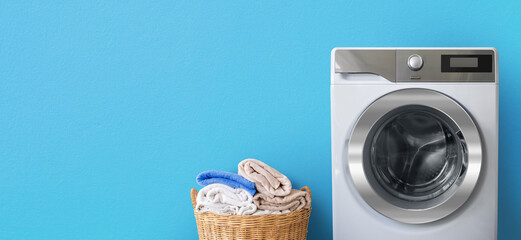 Washing machine with laundry near clean bath towels in wicker basket on blue wall background-Copy space for text