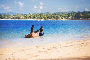 two young men fishing on white sandy beach from the boat in white water on the island