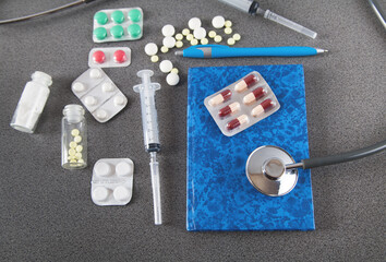 Fototapeta na wymiar Doctors desk. Stethoscope, notebook and pills, on gray background. Concept of medicine.