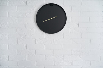 Minimalistic black clock on a white brick wall in the interior