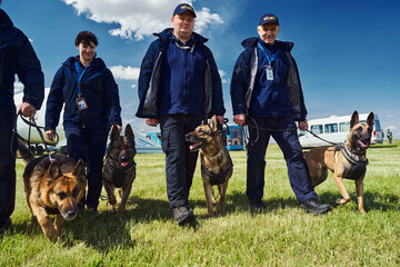 Cheerful security officers with detection dogs walking down airfield