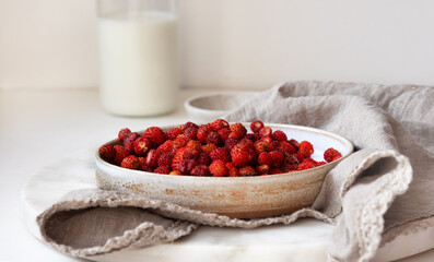 Strawberry breakfast in a ceramic plate bowl with a milk jar in the background. Food photo in a light key.