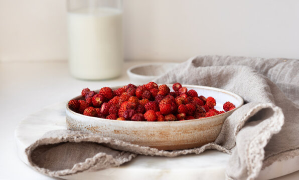 Strawberry breakfast in a ceramic plate bowl with a milk jar in the background. Food photo in a light key.