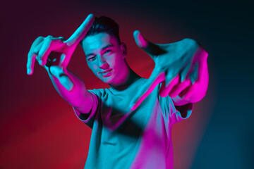 Gesturing. Portrait of Caucasian young man posing isolated on dark red studio background in neon pink light. Concept of human emotions, facial expression. © master1305