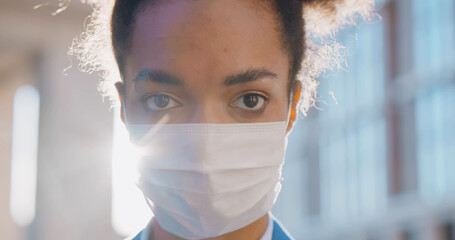 Portrait of afro young businesswoman wearing medical mask standing outside office building