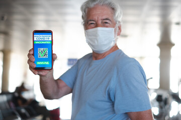 Fototapeta na wymiar Senior traveler in airport showing green pass vaccination passport on mobile phone waiting for departure of flight. Coronavirus and freedom concept