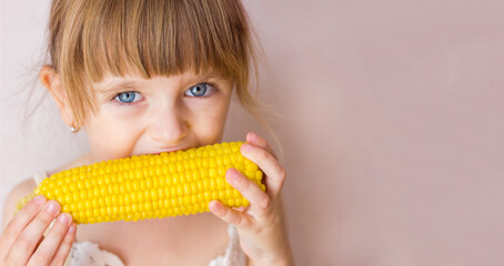 Close-up portrait of a little beautiful girl with blue eyes and boiled corn in her hands, girl...