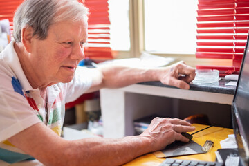 Senior caucasian man looking at computer surfing the net. Home inside window, curiosity