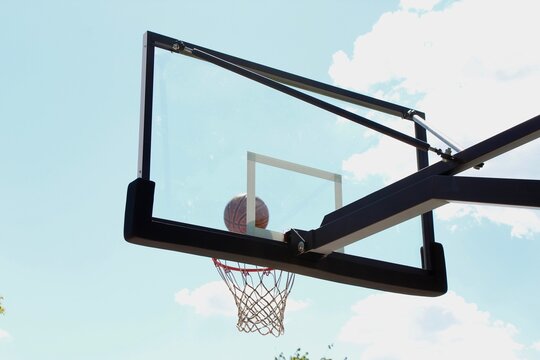 A ball hits basketball hoop attached to the glass basketball backboard