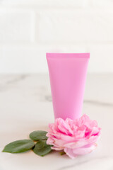 pink tube with rose face or body cream or scrub decorated with pink core flowers. Skin care concept. Unbranding mockup