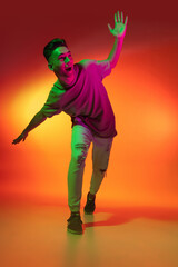 Portrait of Caucasian young man dancing, dancing isolated on orange studio background in neon light. Concept of human emotions, facial expression.