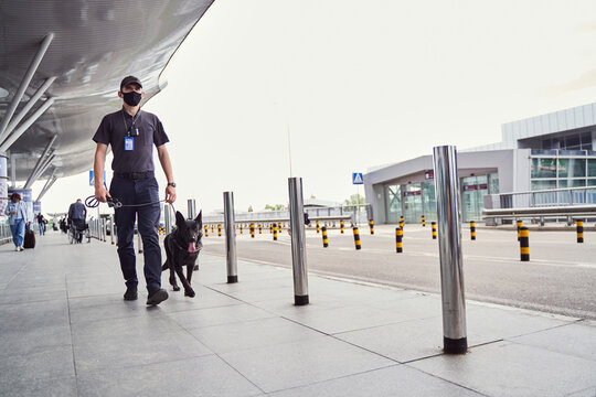 Security Officer With Detection Dog Walking Outdoors At Airport