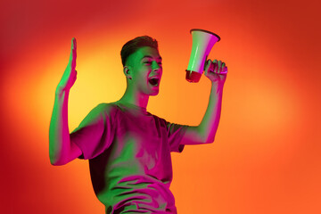 Portrait of Caucasian young man shouting with joy isolated on orange studio background in neon light. Concept of human emotions, facial expression.