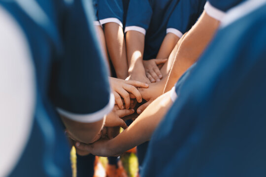 Sports team stacking hands together in a group. Happy children teammates motivated in a team. Team building activities and boosting sports players' morale. Schoolboys building team spirit before game