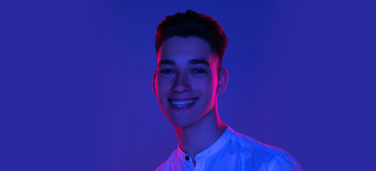 Close-up Caucasian young man posing isolated on blue studio background in neon pink light. Concept...