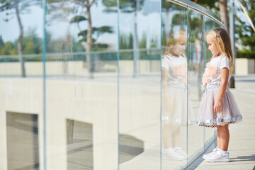 A little blonde girl in a white t-shirt and pink skirt looks over the glass railing at the spectacle.