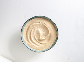 Humus en cuenco sobre fondo blanco, vista cenital. Hummus in bowl on white background, overhead view.