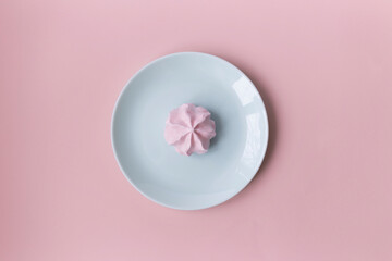 Top view of one pink meringue on the light blue plate on the pink background with copy space