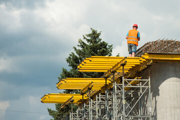 A worker in a protective helmet on concrete columns installs a reinforced frame during the construction of a road bridge