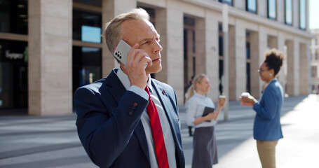 Portrait of cheerful businessman talking on mobile phone while standing near modern office.