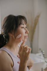 Beautiful asian woman doing face massage with pink quartz roller during daily beauty morning routine