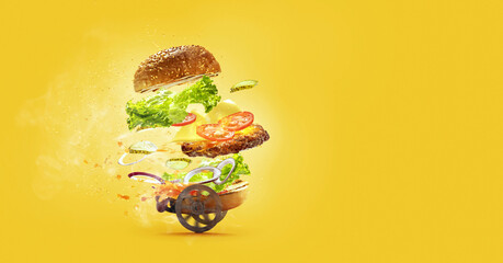 Hamburger with flying ingredients on yellow studio background. Fast food, cuisine and express...