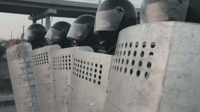 Tilt up slowmo shot of riot police officers in full gear holding their shields and blocking street