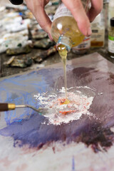 Artist pouring oil into color and texture to mix with a spatula over linen and add to the surface of a painting. Professional master painter arranges and mixes materials to add to the artwork