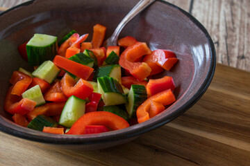 Salad with cucumbers and red peppers marinated in olive oil and served in a rustic enamel bowl with fork