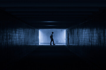 Fototapeta na wymiar Dark underground passage with a silhouette of a man in profile in cold colors.
