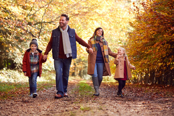 Family With Mature Parents And Two Children Holding Hands Walking Along Track In Autumn Countryside