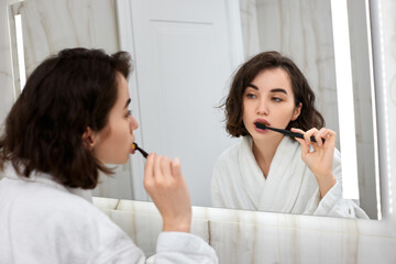 woman in white bathrobes brushing teeth in front of mirror