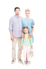 Vertical full length shot of young adult parents wearing casual clothes standing with their sad little daughter, white background