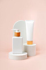 Fototapeta na wymiar Cream tube and pump bottle mockup on podium with arch on beige background. Natural skincare beauty product. Branding and packaging presentation.