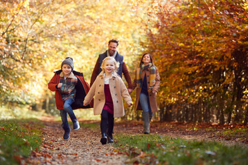 Family Walking Along Track In Autumn Countryside With Children Running Ahead
