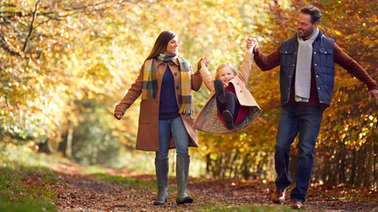 Excited Girl Being Swung By Parents On Family Autumn Walk Through Countryside