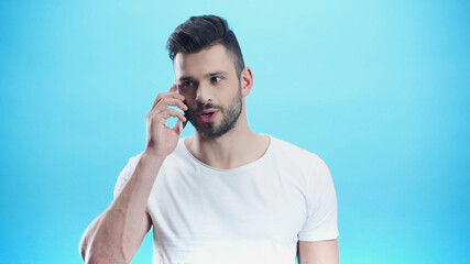 concentrated man talking on mobile phone isolated on blue