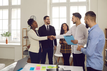Male boss shakes hands with woman congratulating successful employee with good project performance, hiring intern welcome in group while business team support colleague with smile. Creative office - obrazy, fototapety, plakaty