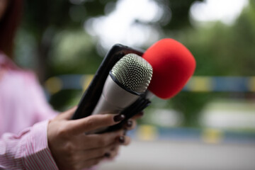 Professional journalist at event, holding microphones and recording notes on smartphone